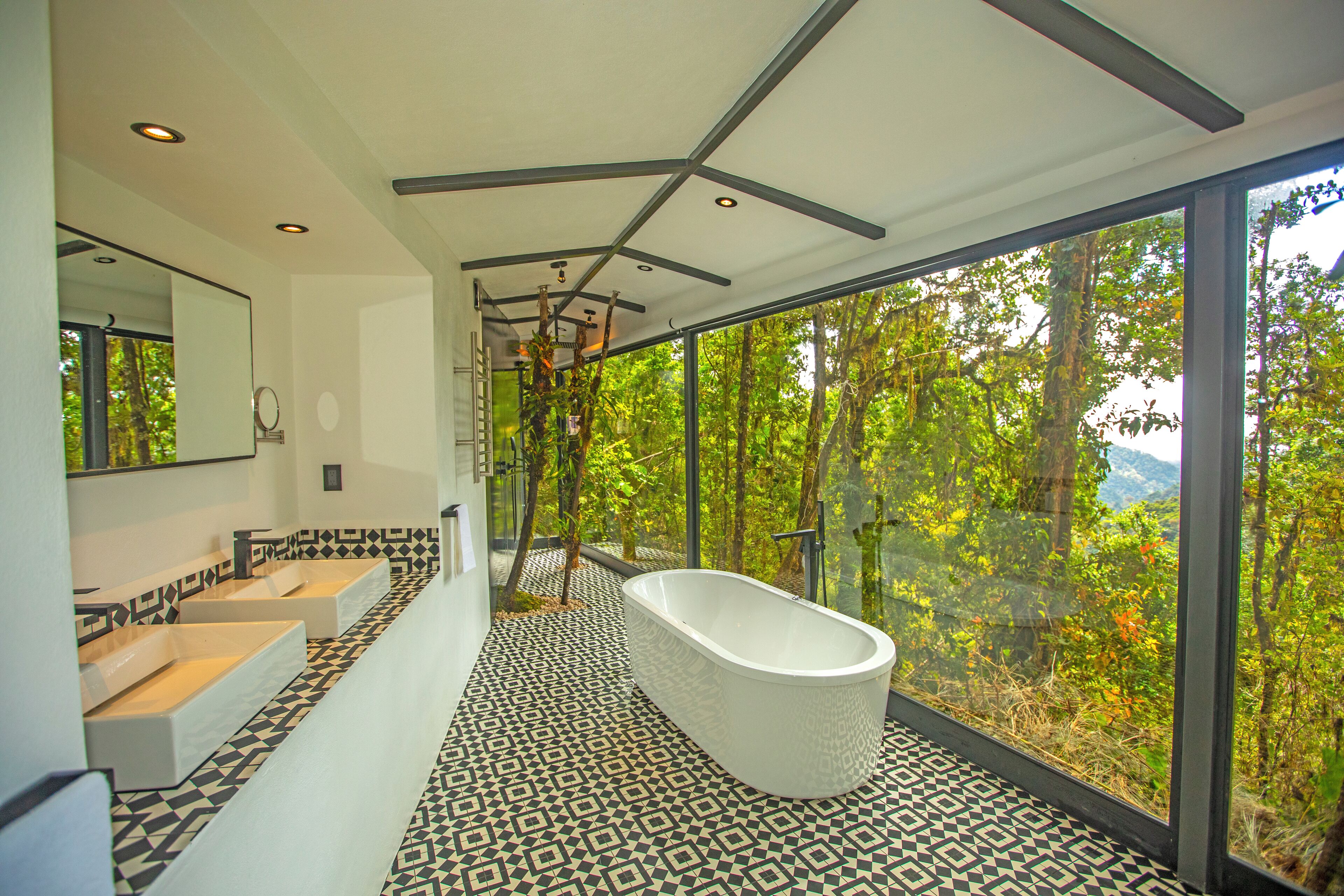 A modern bathroom with a freestanding bathtub, large windows, and patterned floor tiles.