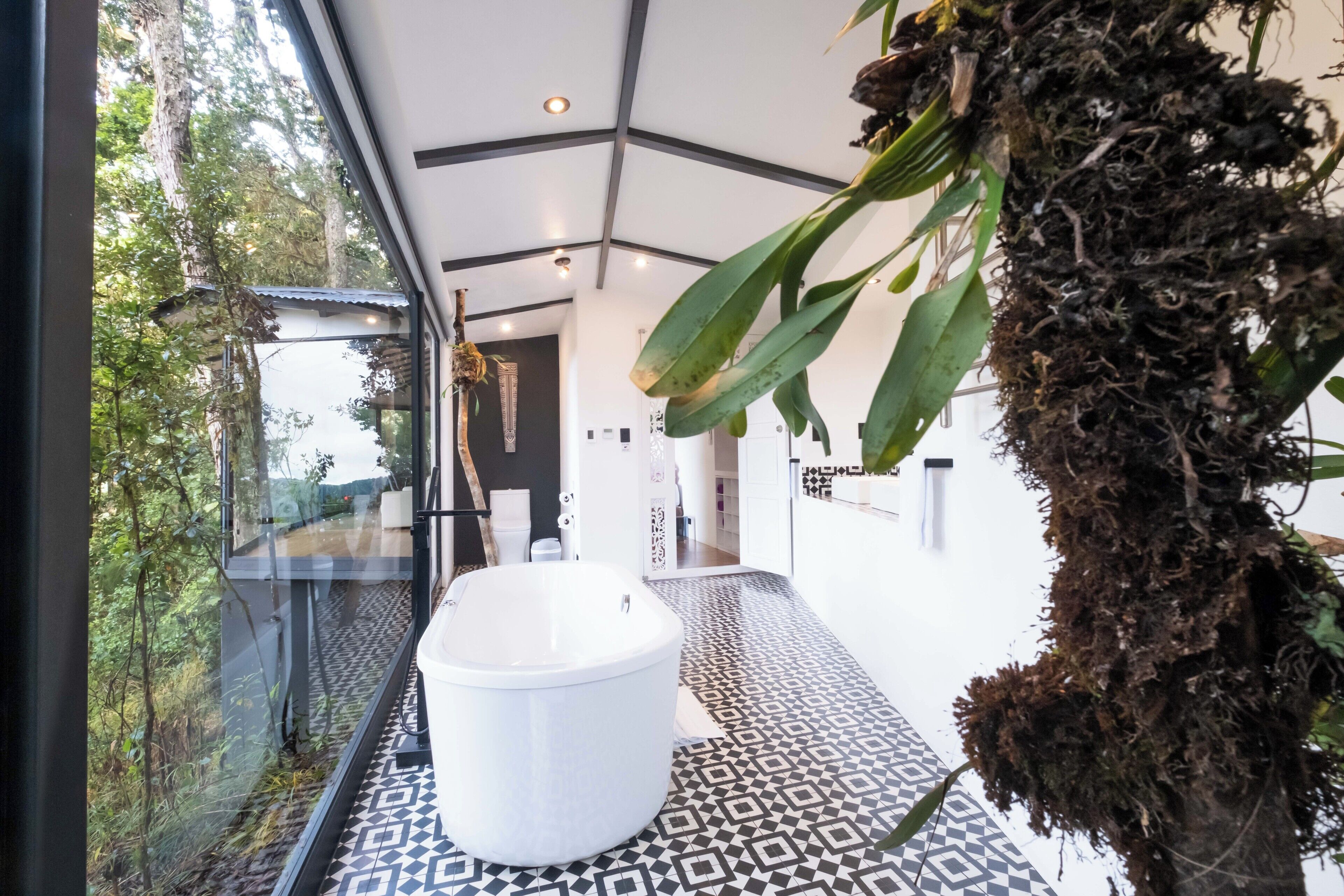 A modern bathroom with a large bathtub, patterned floor tiles, and a view of the outdoors through a glass wall.