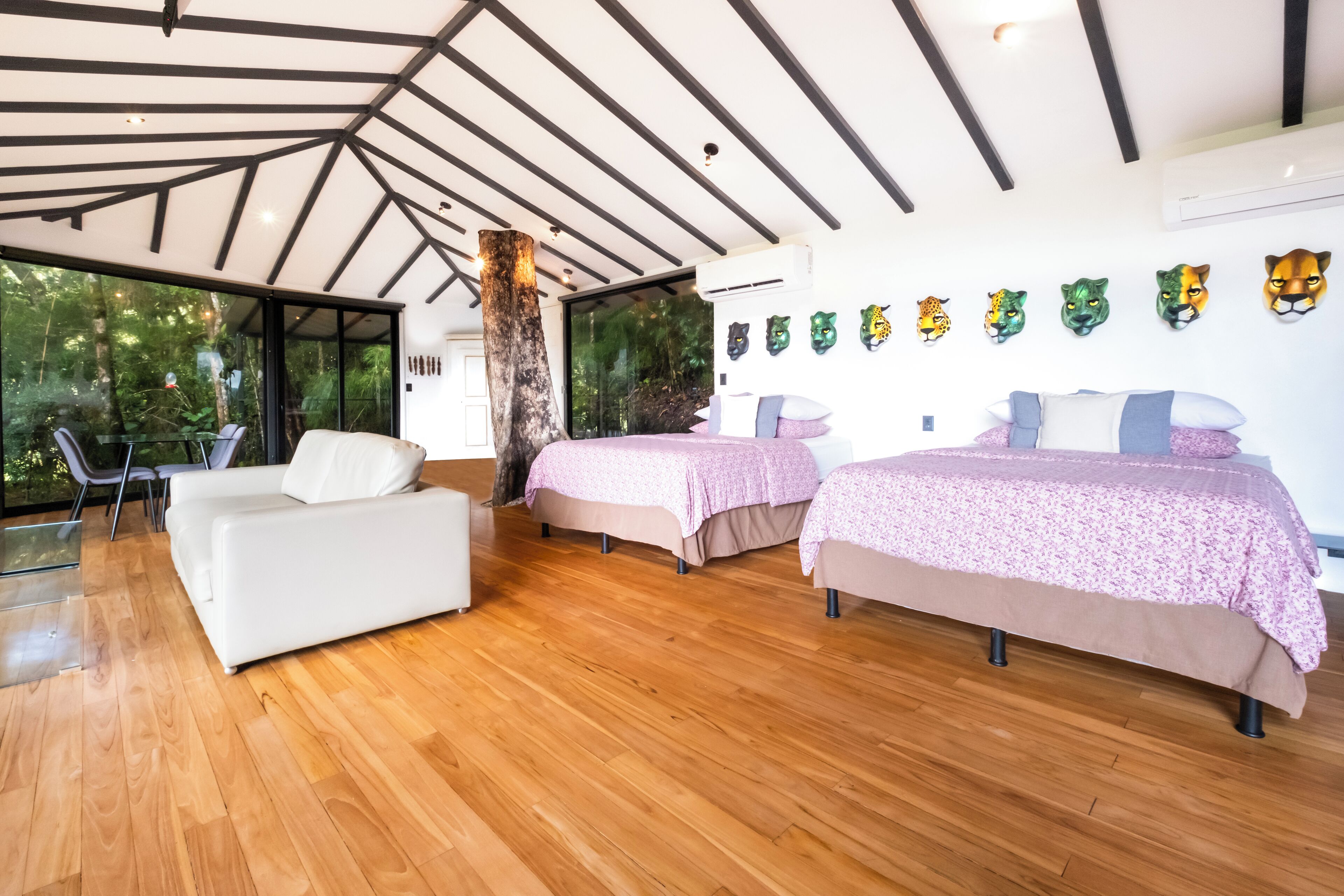 A modern bedroom with two beds, a white sofa, and a large window overlooking greenery.