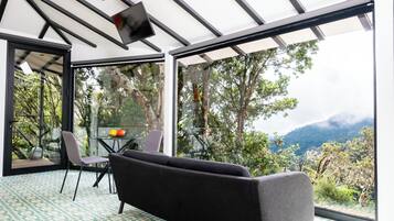 Un espacio habitable moderno y abierto con sofá y sillones, ventanas amplias que ofrecen vistas a un paisaje montañoso.