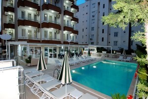 Una piscina con sillones de descanso y sombrillas, rodeada por un edificio con varios balcones y una zona de bar.