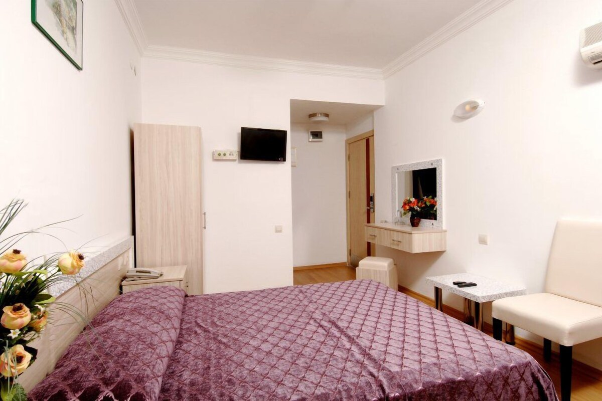 Un dormitorio con cama, una silla, una mesita, un televisor y un espejo.