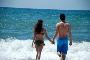 Ein Paar geht Hand in Hand am Strand, wo Wellen brechen.