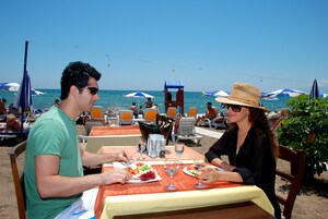 Un restaurante frente a la playa con terraza, mesas y sombrillas.