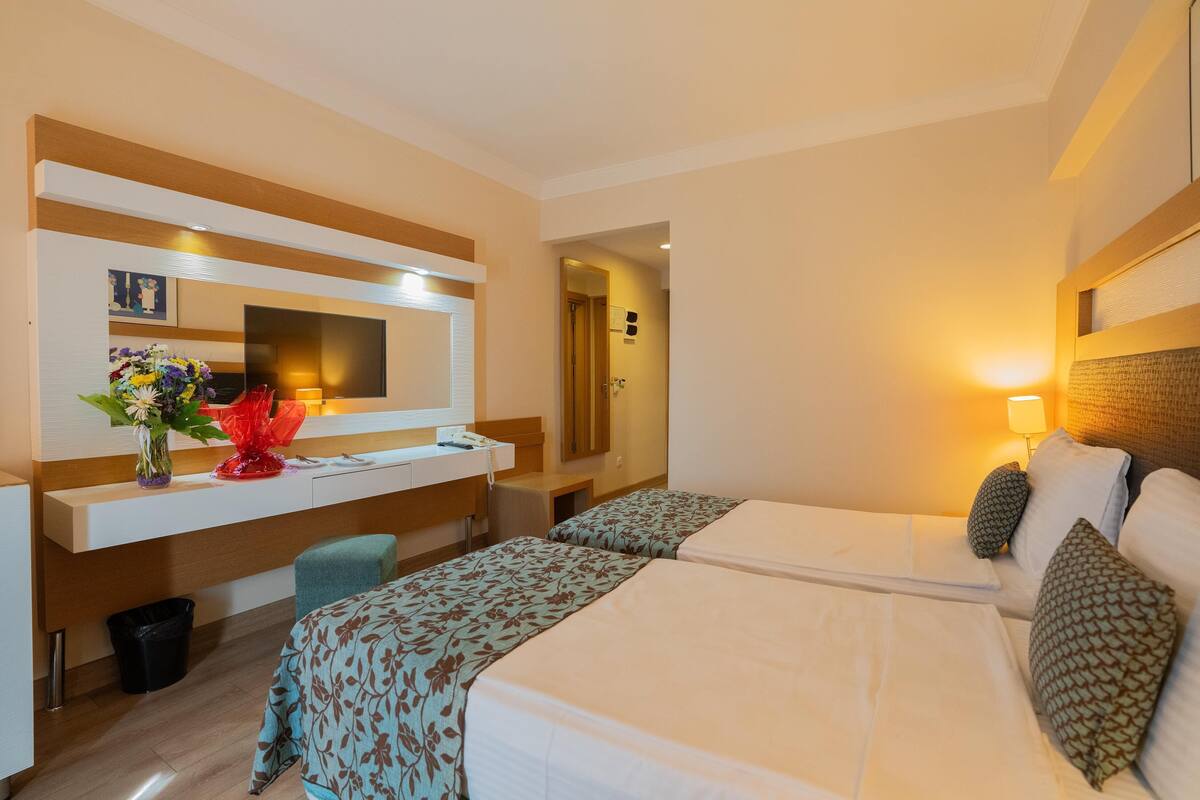 Habitació d'hotel amb dos llits, un escriptori amb mirall, un ram de flors i un gresol.