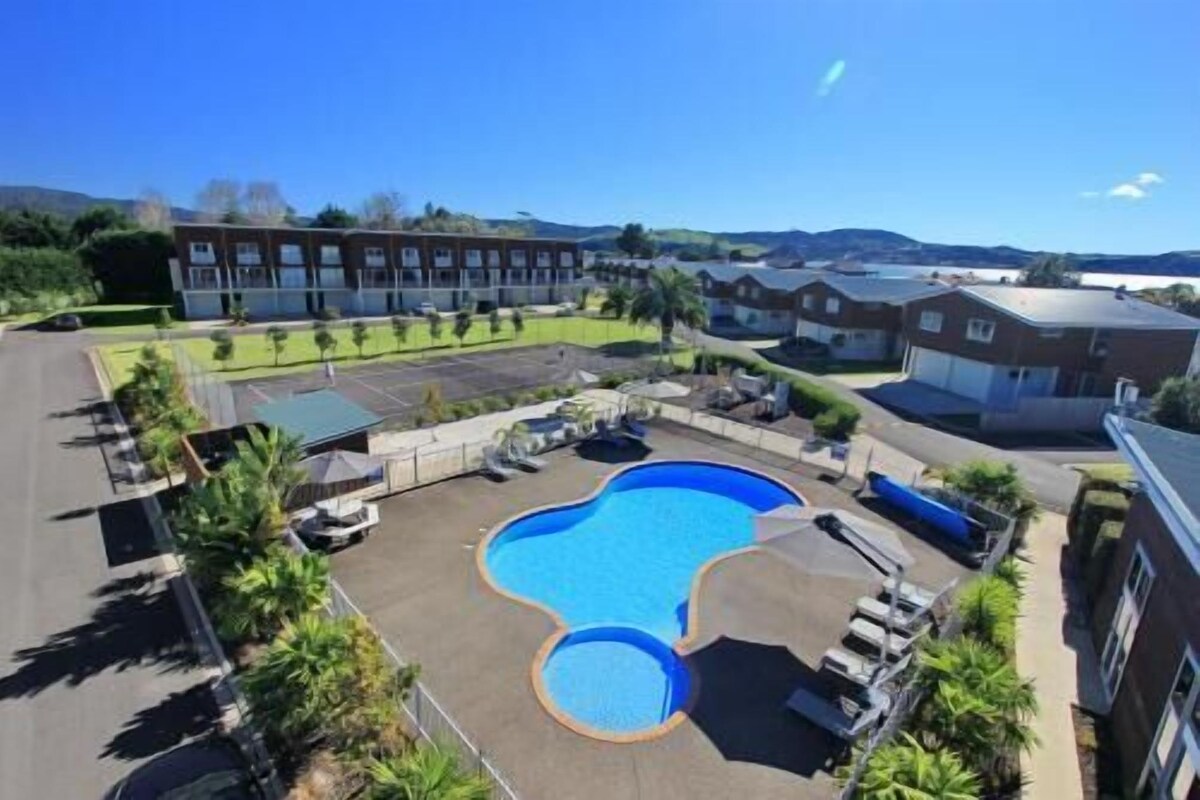 A pool area with a unique shape, surrounded by buildings and greenery.