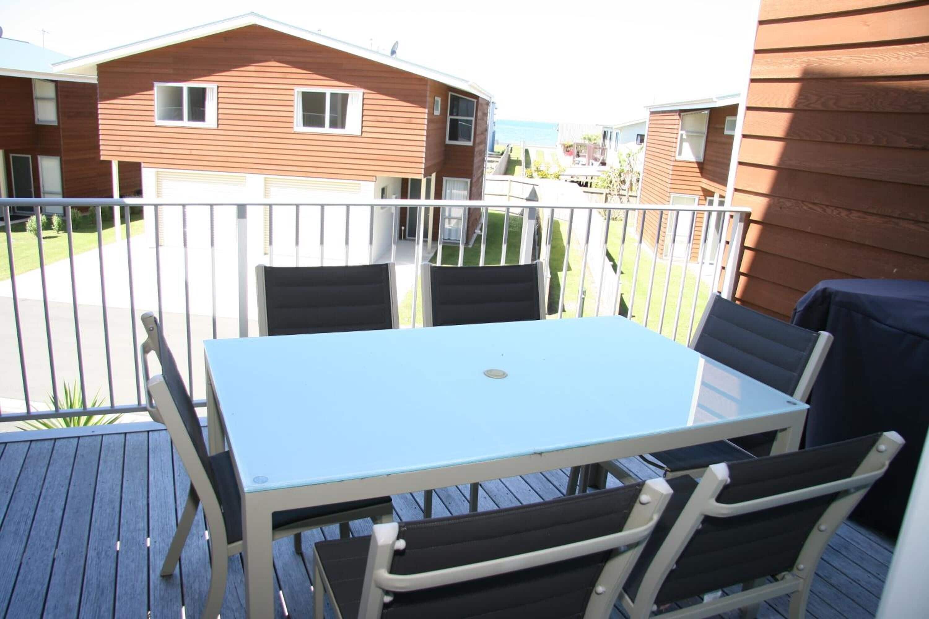 Un balcón con mesa y sillas, con vistas a un barrio residencial con casas.