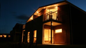 Una casa moderna de dos pisos con balcón, ventanas amplias y luz cálida en el interior.