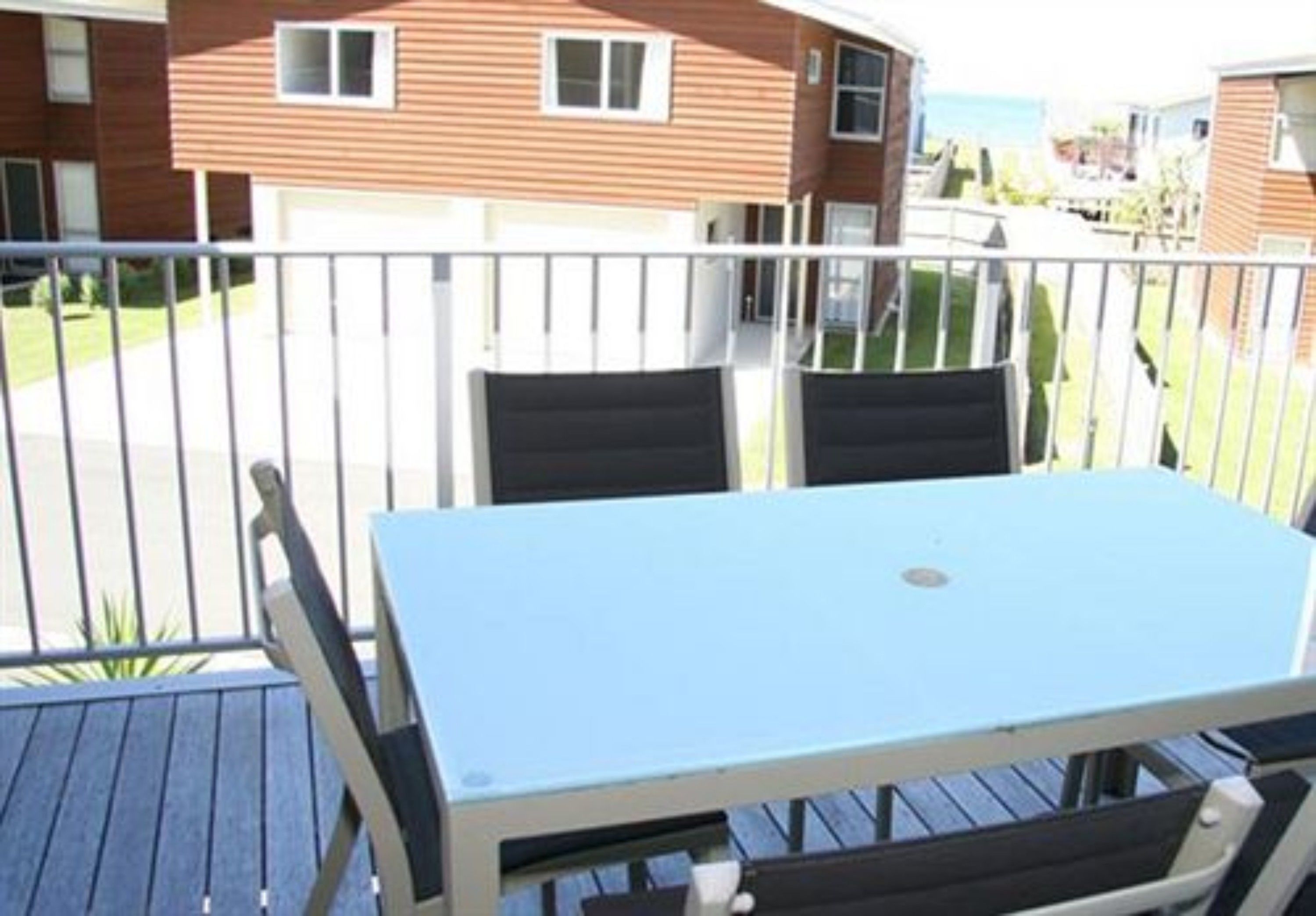 A balcony with a table and chairs, overlooking a residential area with houses and a clear sky.