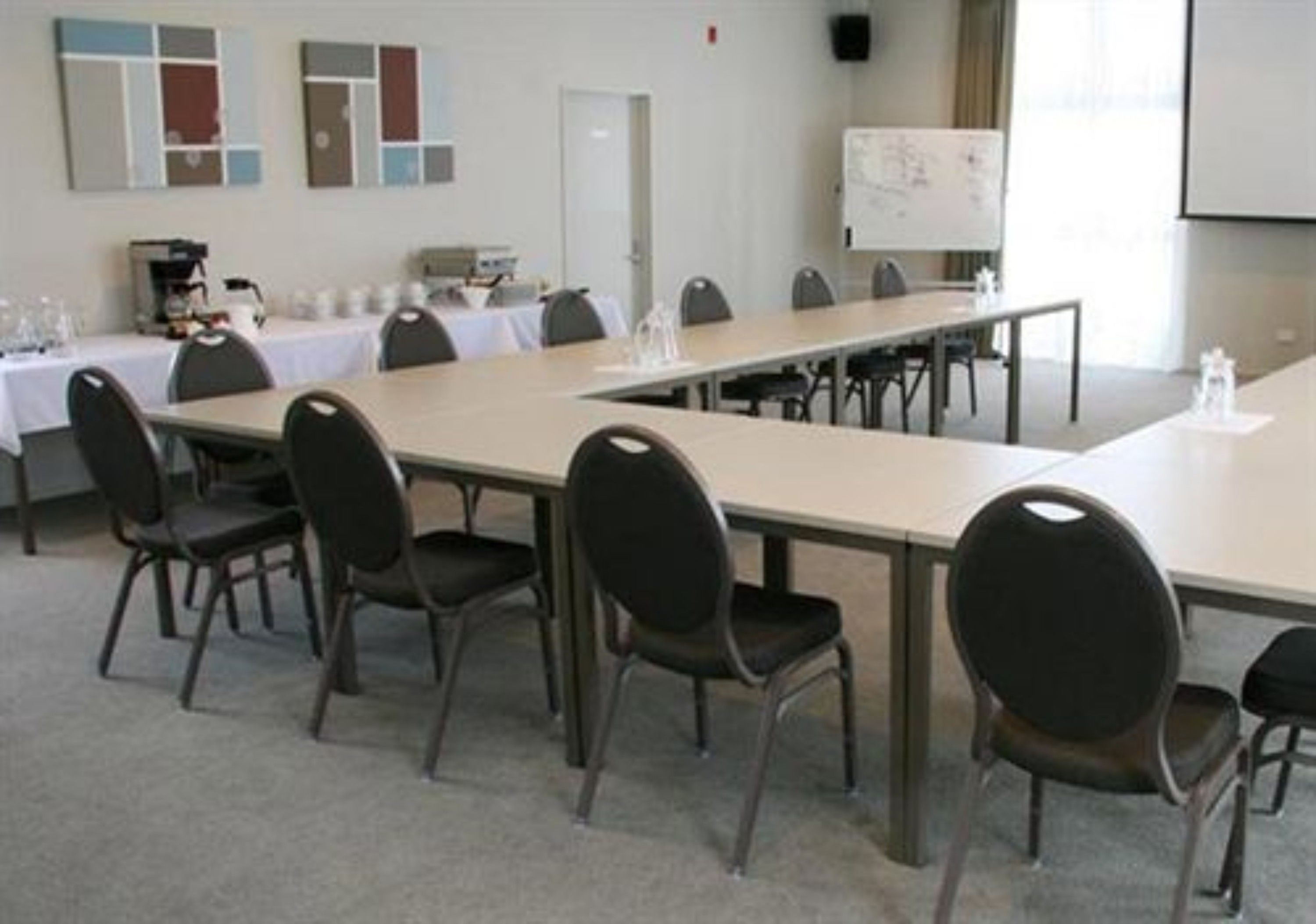 A conference room with a long table, chairs, a whiteboard, and a projector screen.