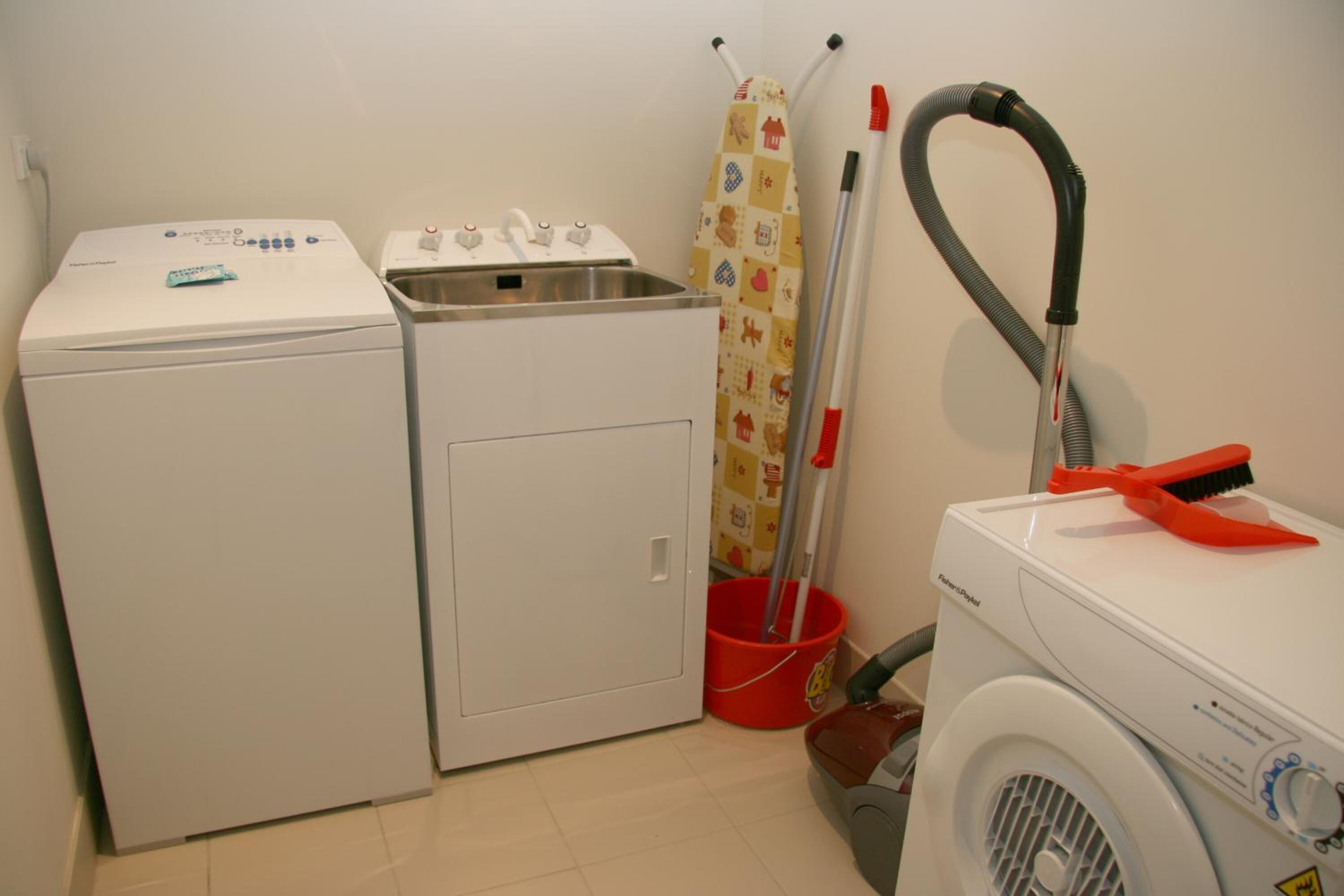 Un área de lavandería con lavadora, secadora, lavabo y utensilios de limpieza.