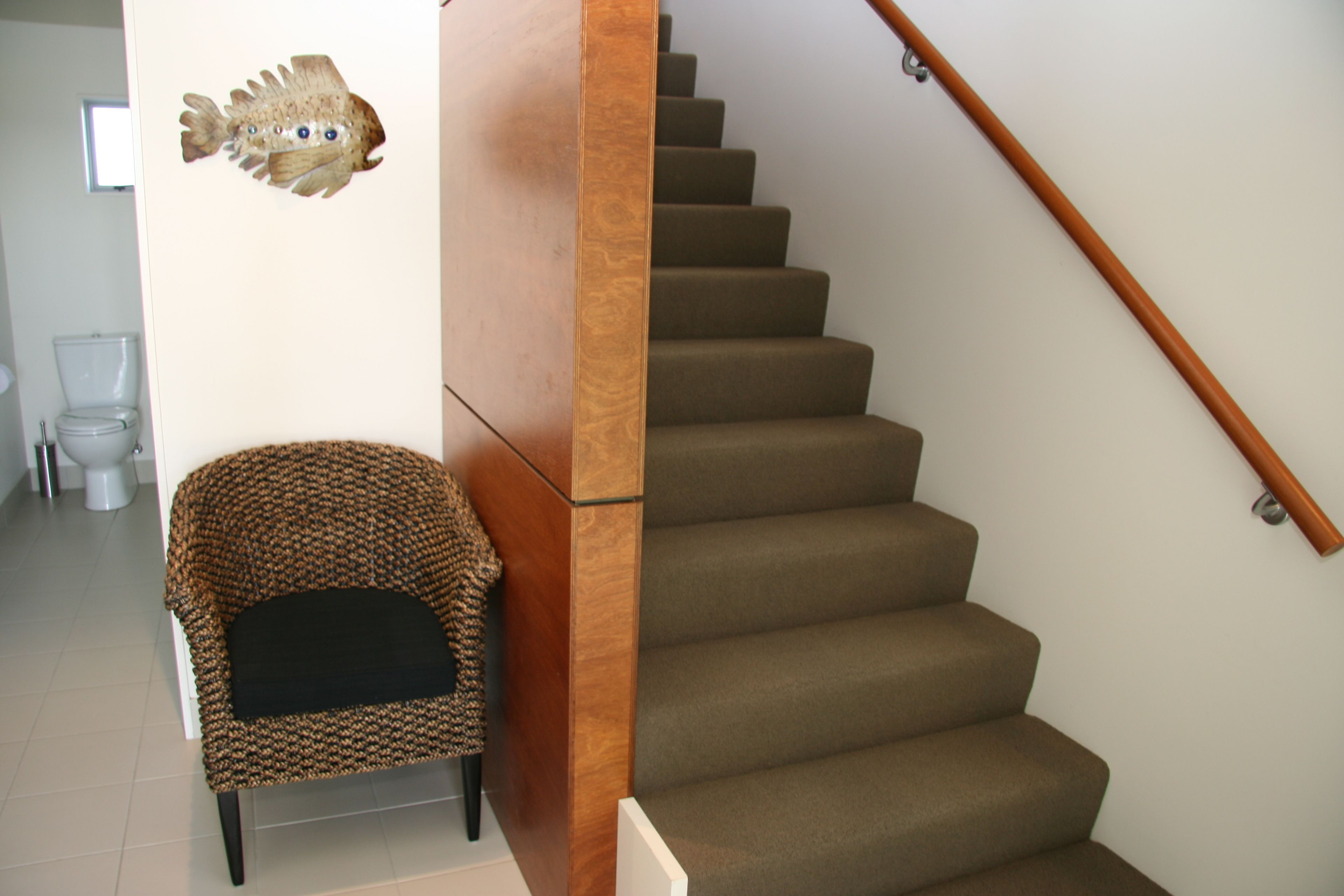 Un escalier dont les marches sont recouvertes de moquette et qui possède une main courante en bois.