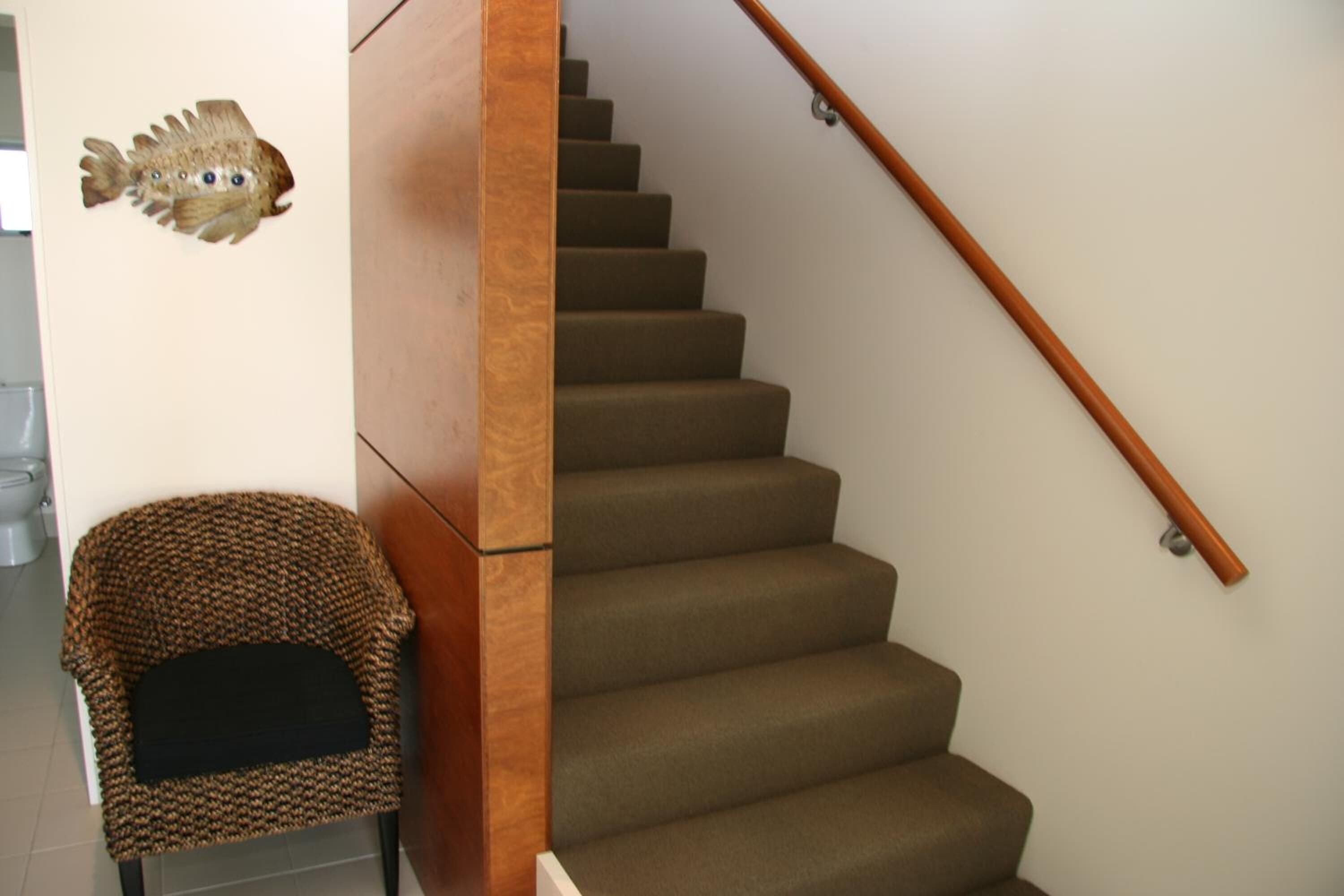 A staircase with a wooden handrail, carpeted steps, and a wall-mounted fish decoration.
