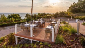 An outdoor dining area with tables and chairs, overlooking a body of water. - Hotel Bernstein (Sellin)