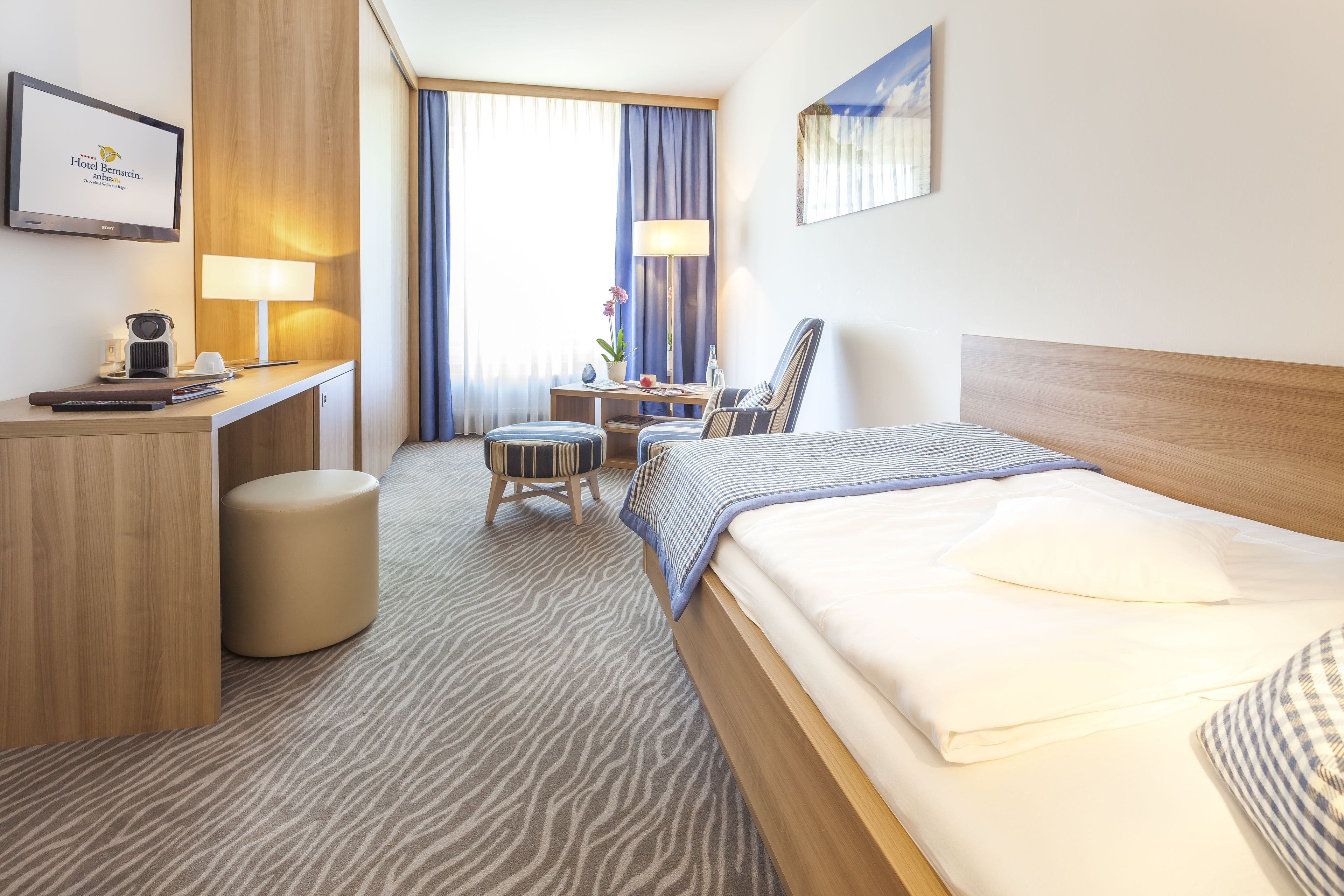 Een hotelkamer met een bed, bureau, stoel en een klein tafeltje met een lamp.