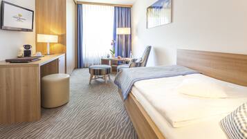 Een hotelkamer met een bed, bureau, stoel en een klein tafeltje met een lamp.