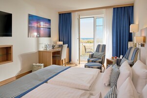 Habitación de hotel con dos camas, un escritorio, una silla y un balcón con vistas.