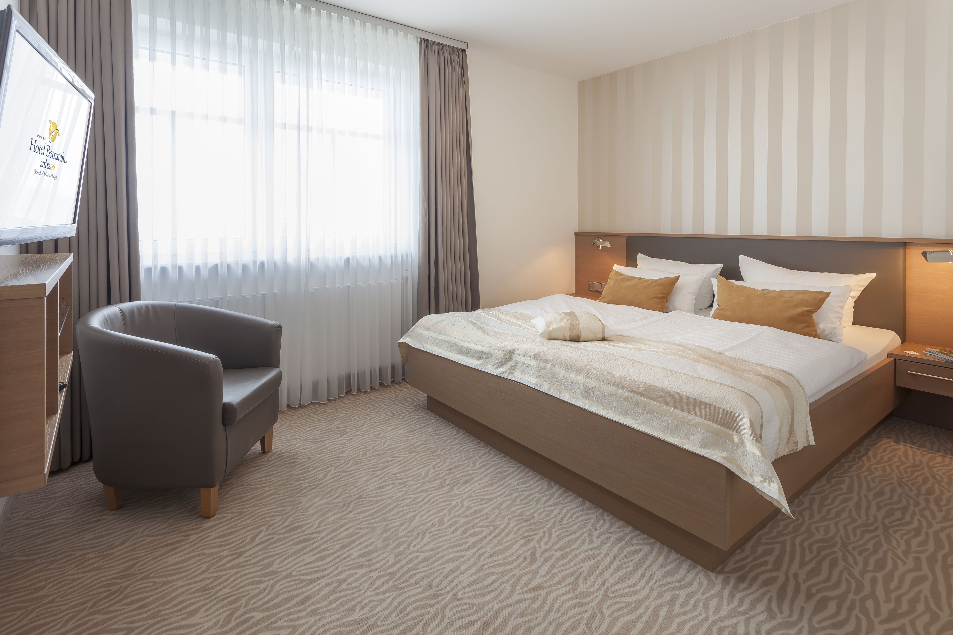 Una camera d'albergo con un letto grande, una sedia, una TV e una finestra con tende.