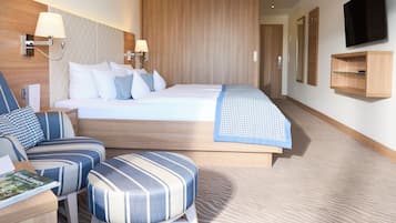 A modern hotel room with a large bed, a seating area with striped chairs, a flat-screen TV mounted on the wall, and a wooden wardrobe.