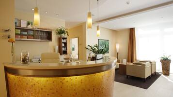 A reception area with a curved counter, a seating area with two sofas, a potted plant, and a bookshelf.