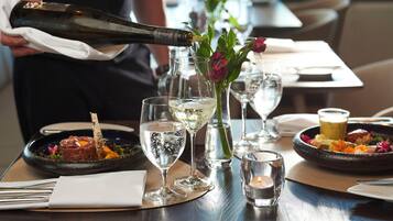 A dining table with a bottle of champagne being poured into a glass, surrounded by plates of food and glasses of water.