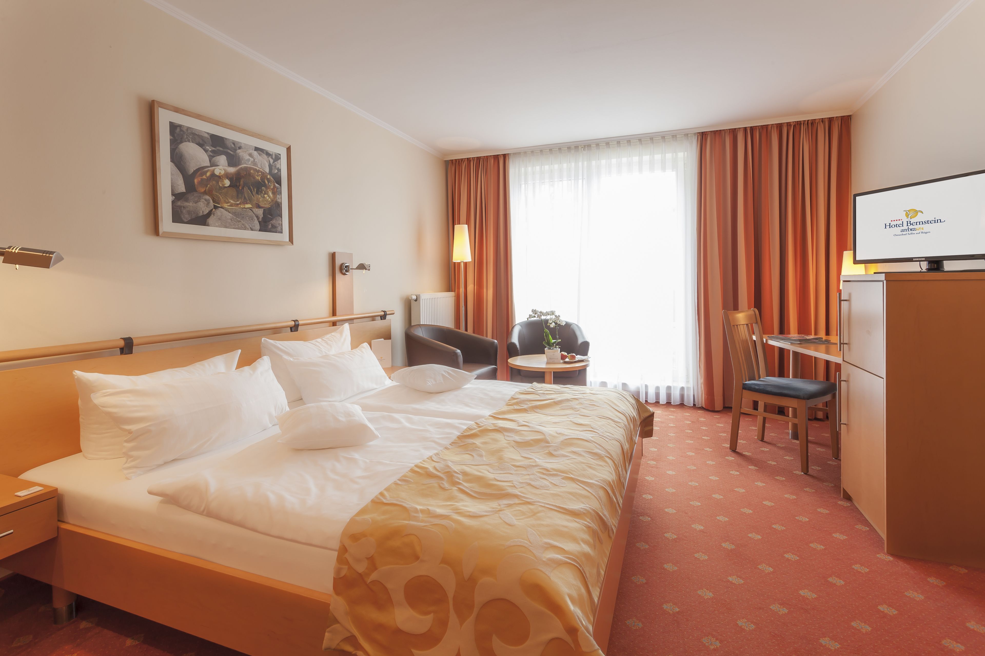 Ein Hotelzimmer mit Bett, Schreibtisch, Stuhl, Fernseher und einem Fenster mit Vorhängen.