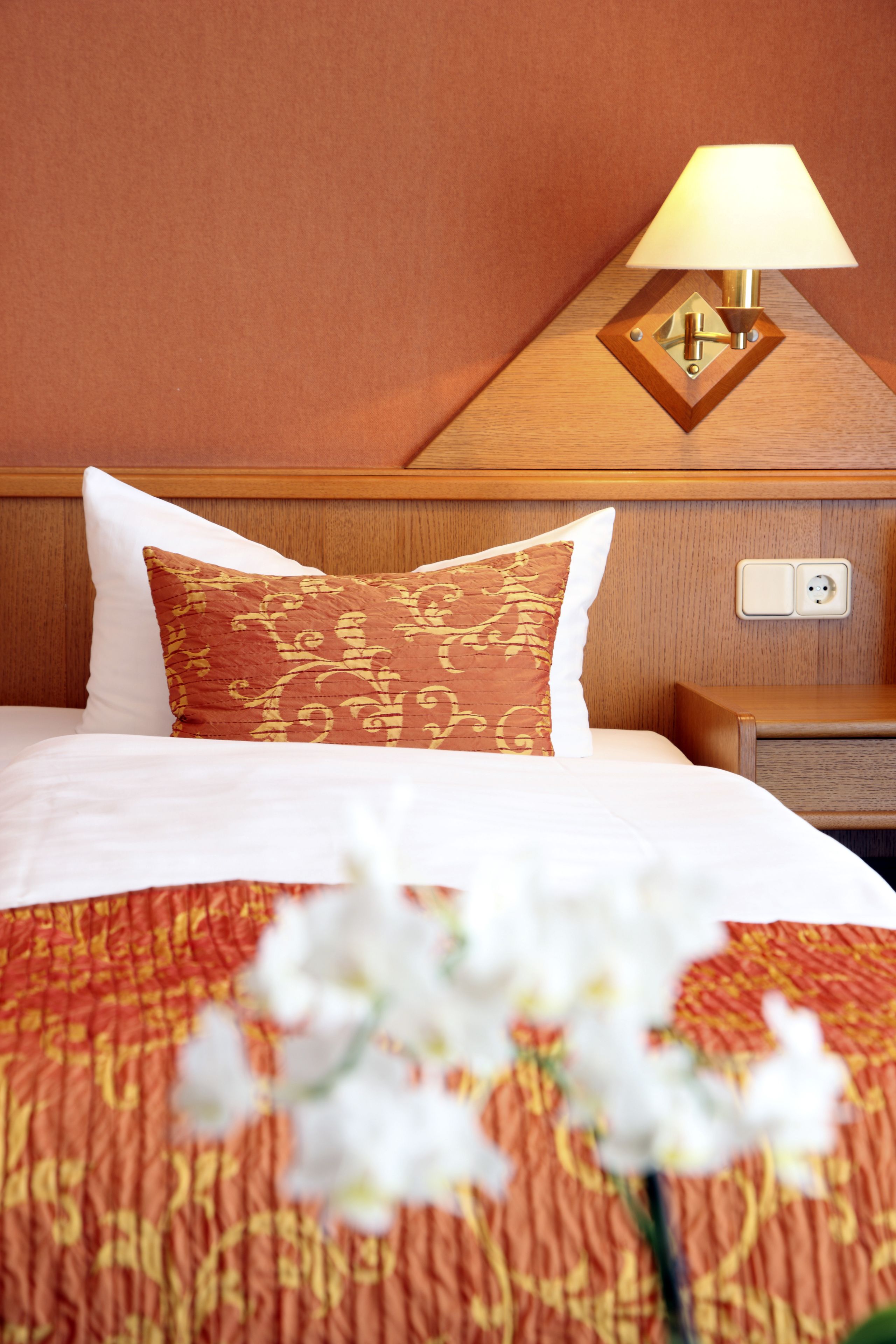 A hotel room with a bed, a nightstand, a lamp, and a power outlet.