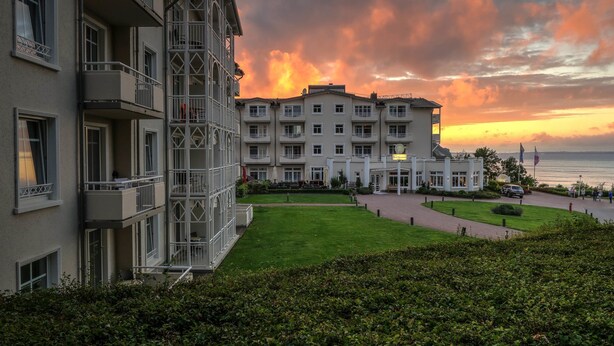 A multi-story hotel with balconies, a well-maintained lawn, and a view of the sea at sunset. - Hotel Bernstein (Sellin)