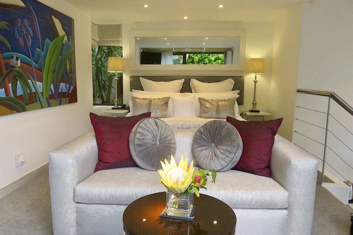 A modern living room with a grey sofa, two decorative pillows, a small table with a vase, and a painting on the wall.