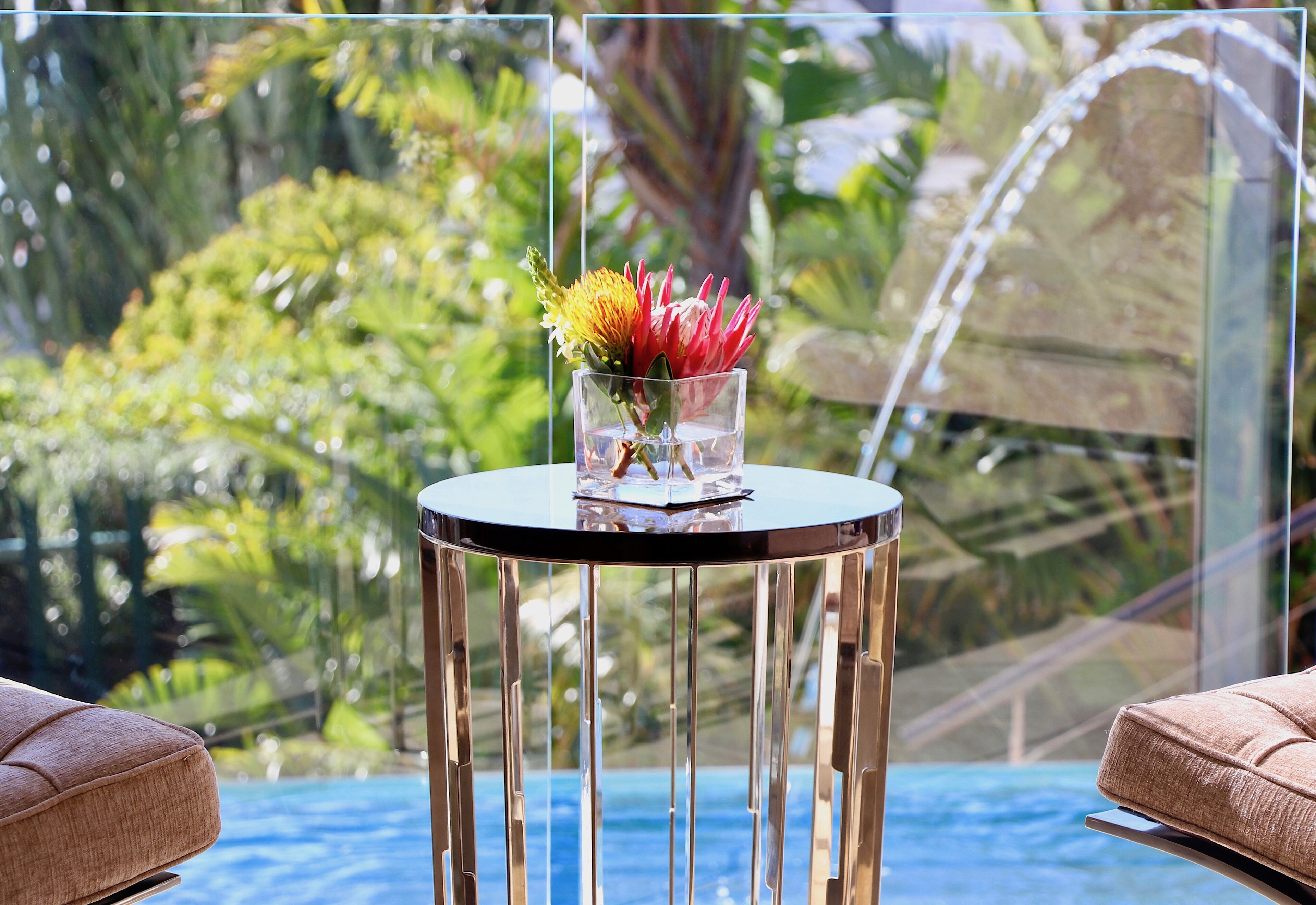 A glass table with a vase of flowers, a pool, and outdoor seating.