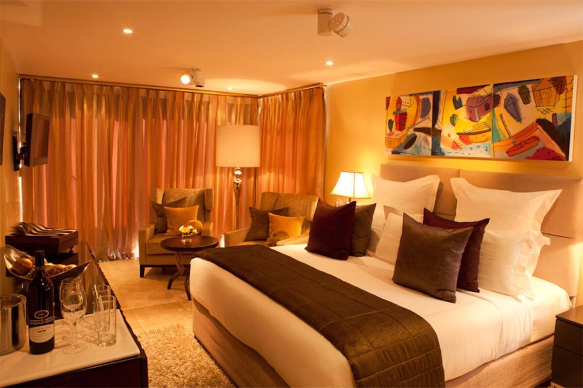 A hotel room with a large bed, a sitting area with a chair and a table, a television, and artwork on the wall.