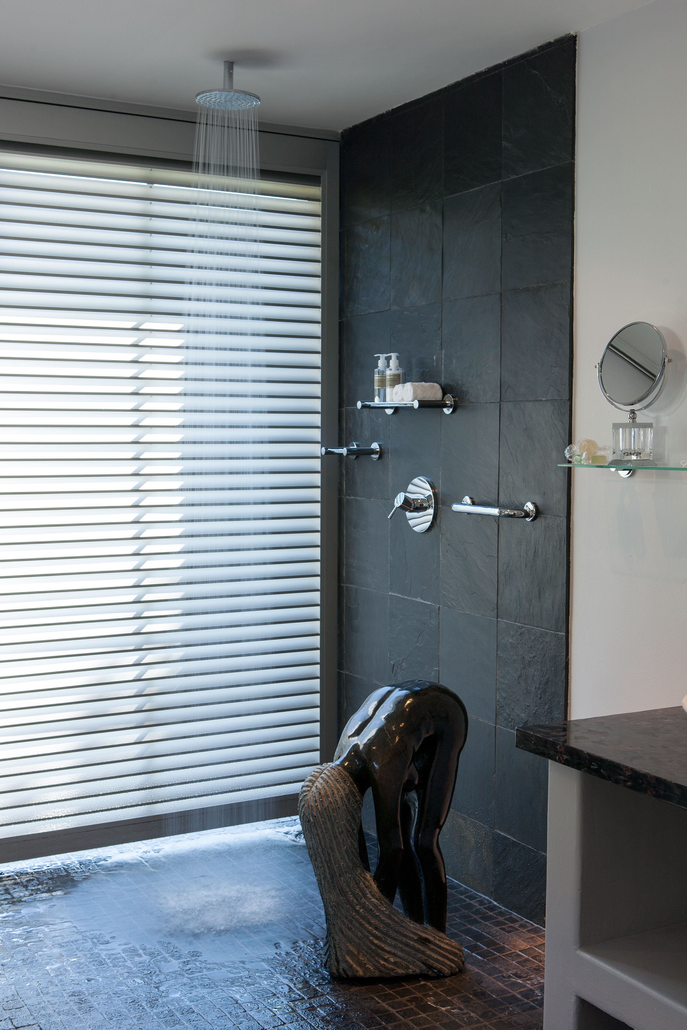A modern bathroom with a shower, a glass shelf with toiletries, and a large mirror.