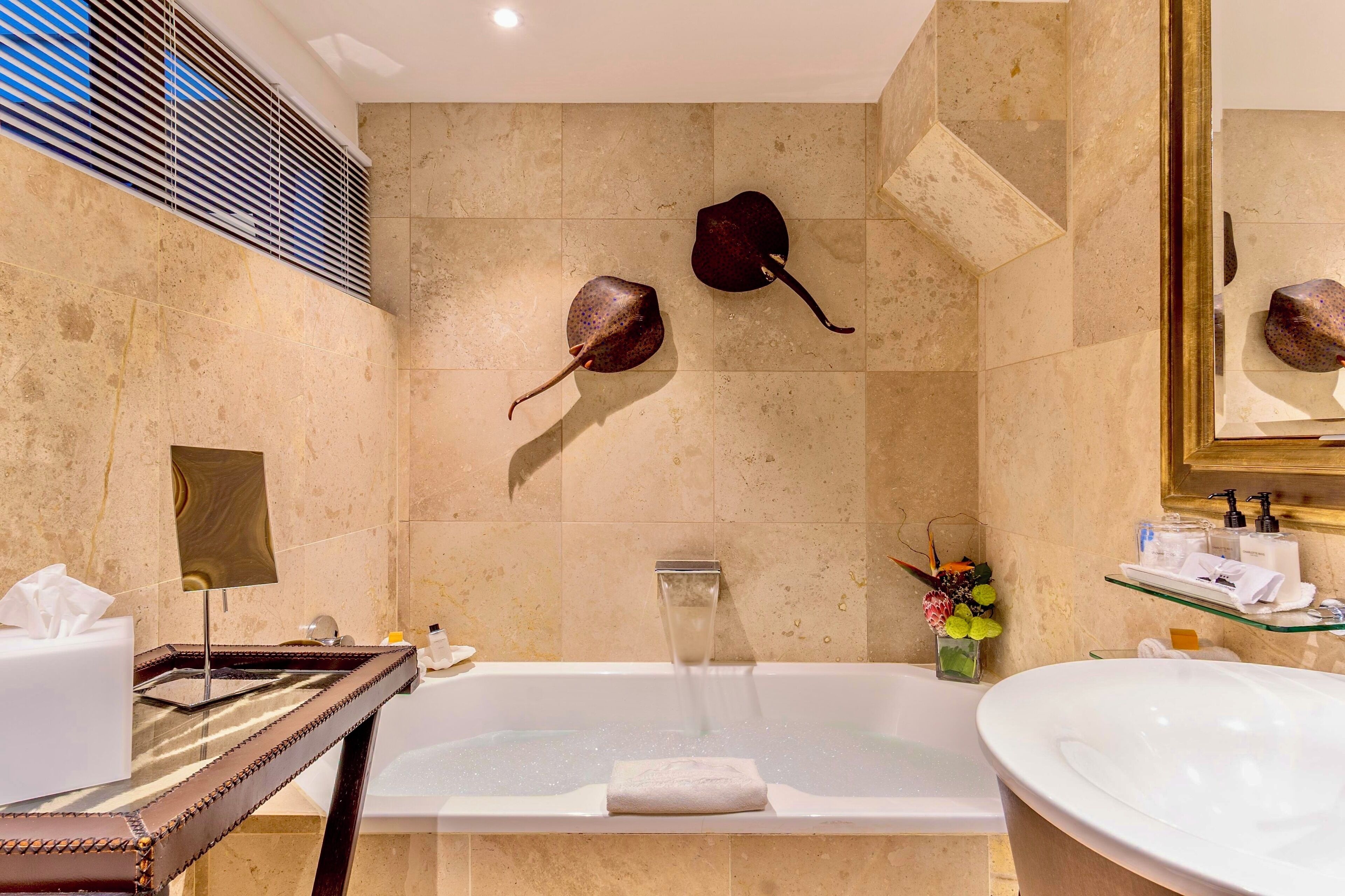 A modern bathroom with a bathtub, a large mirror, and two decorative fish mounted on the wall.