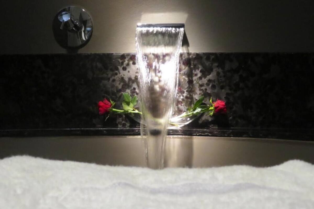 A bathroom with a running water faucet, a mirror, and a floral-patterned wall.