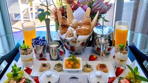 Una mesa de desayuno con diversos alimentos, un jarrón de flores y vista al océano.