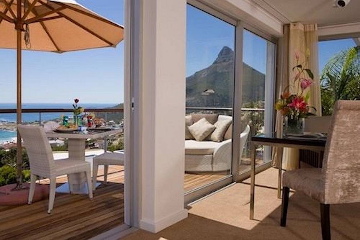 A balcony with a table, chairs, and an umbrella, overlooking a scenic view of the ocean and a mountain.