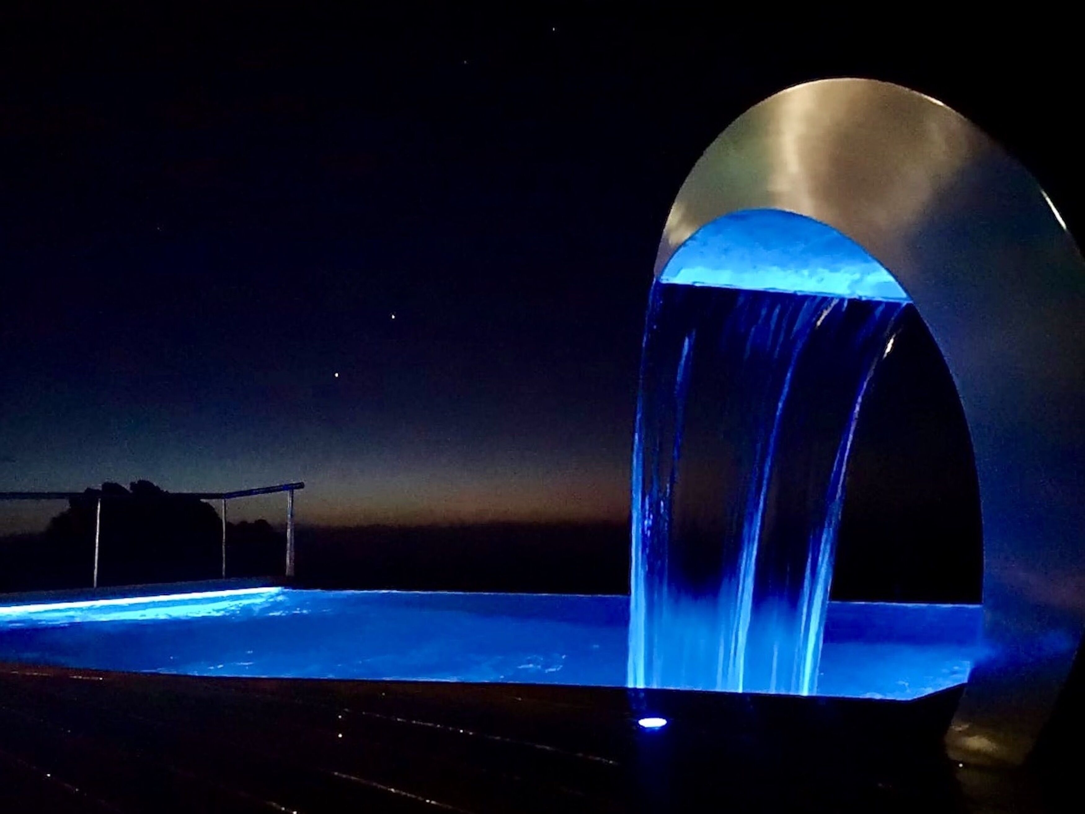 Vue nocturne d’une installation aquatique agrémentée d’une structure arquée métallique.