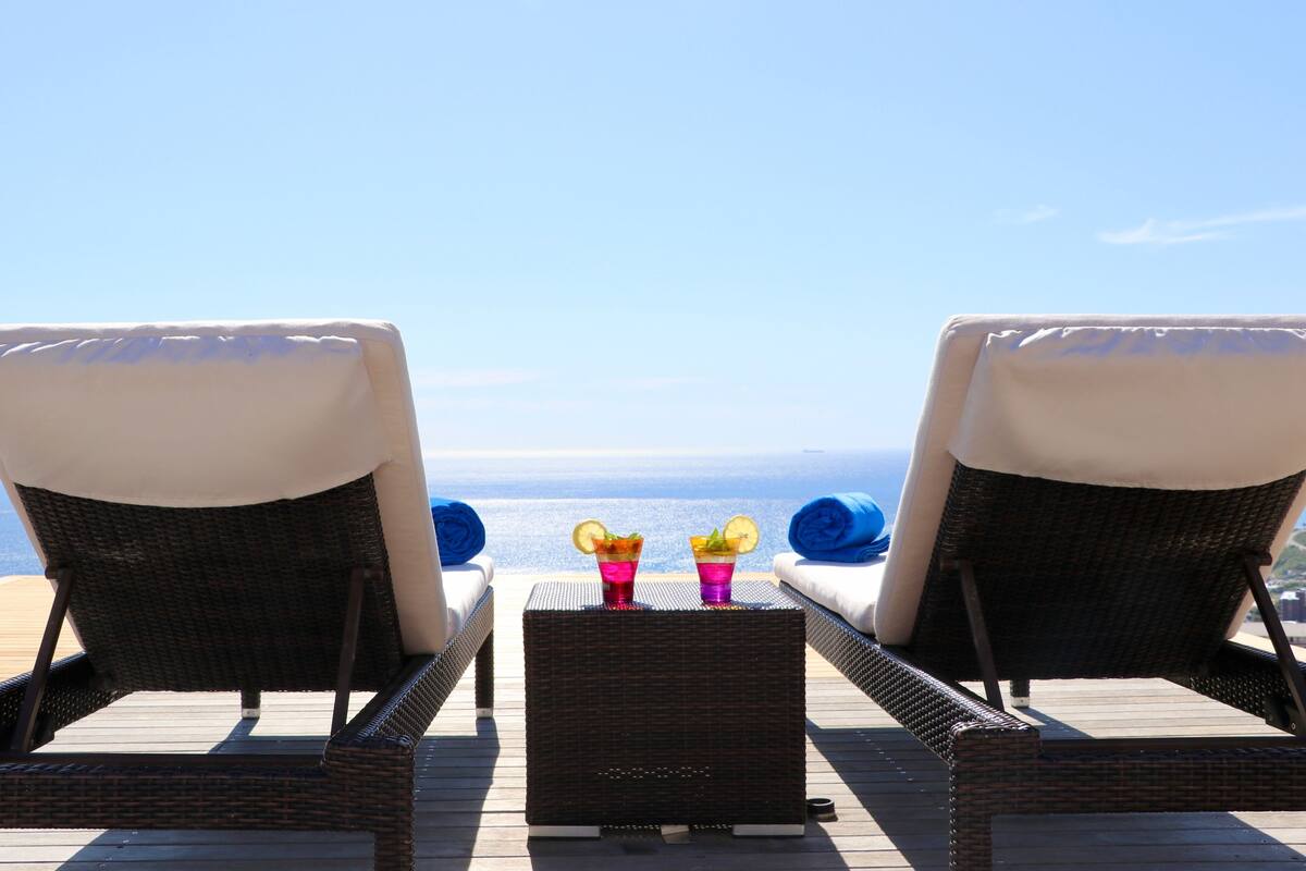 Two wicker lounge chairs with white cushions facing a clear blue sky and ocean view.