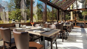 A restaurant with outdoor seating, large windows, and a view of trees. - Hotel Engel (Hamburg)