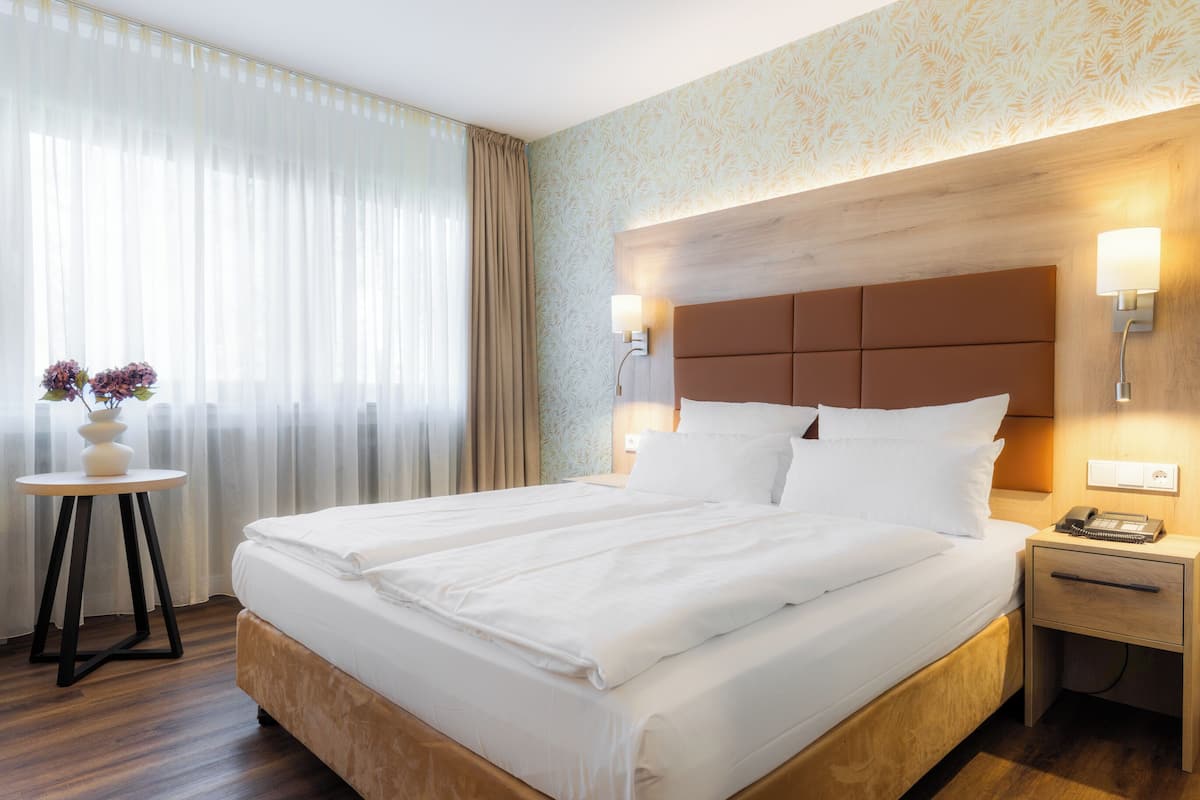 A hotel room with a large bed, bedside tables, a small table with a vase, and a patterned wall.