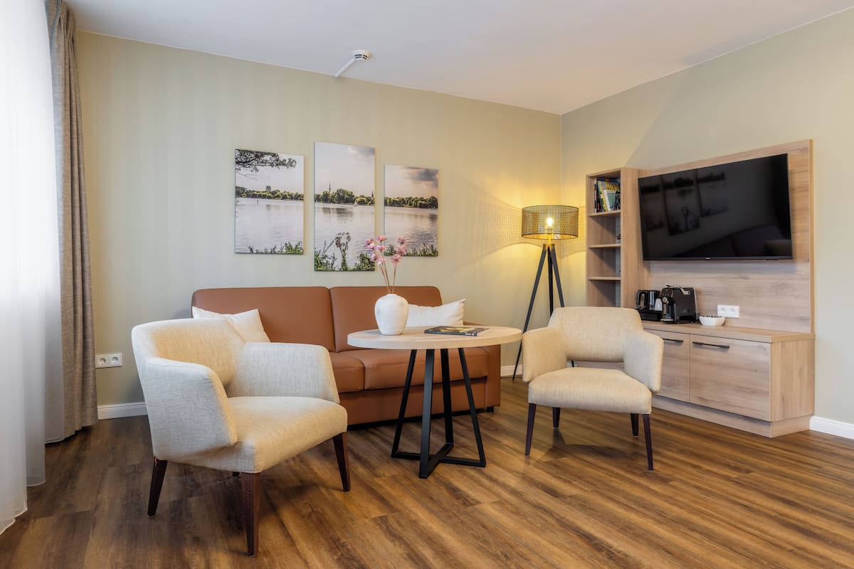 A modern living room with a sofa, two armchairs, a coffee table, a TV, and artwork on the wall.