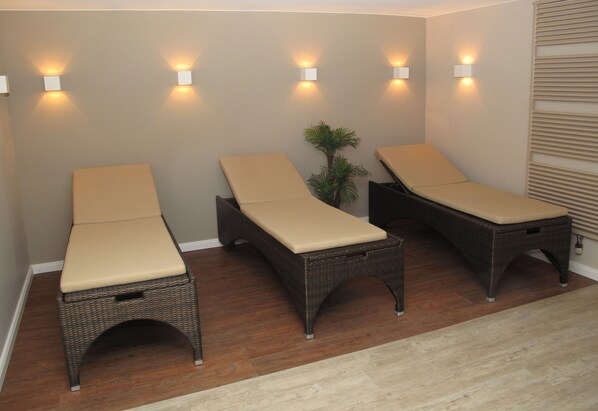 Tres sillones de mimbre con cojines beige frente a una pared, con una pequeña planta entre cada uno.