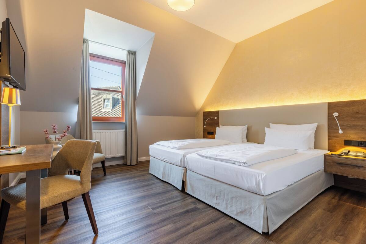 A hotel room with two beds, a desk, a chair, and a window with curtains.