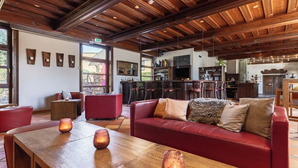 A spacious living area with a wooden ceiling, a red leather sofa, and a wooden coffee table with candles. - Hotel Engel (Hamburg)