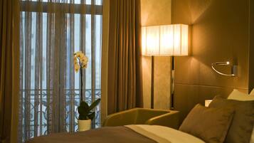 A hotel room with a bed, a bedside lamp, a potted plant, and a window with curtains.