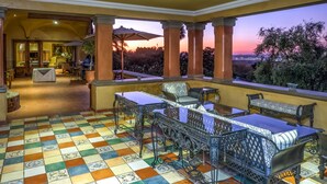 An outdoor patio with checkered flooring, a table with chairs, and a view of the sunset. - Castello di Monte (Pretoria)