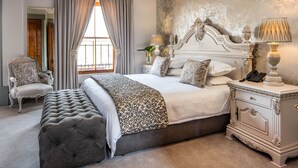 A bedroom with a large bed, a nightstand with a lamp, a chair, and a window with curtains. - Castello di Monte (Pretoria)