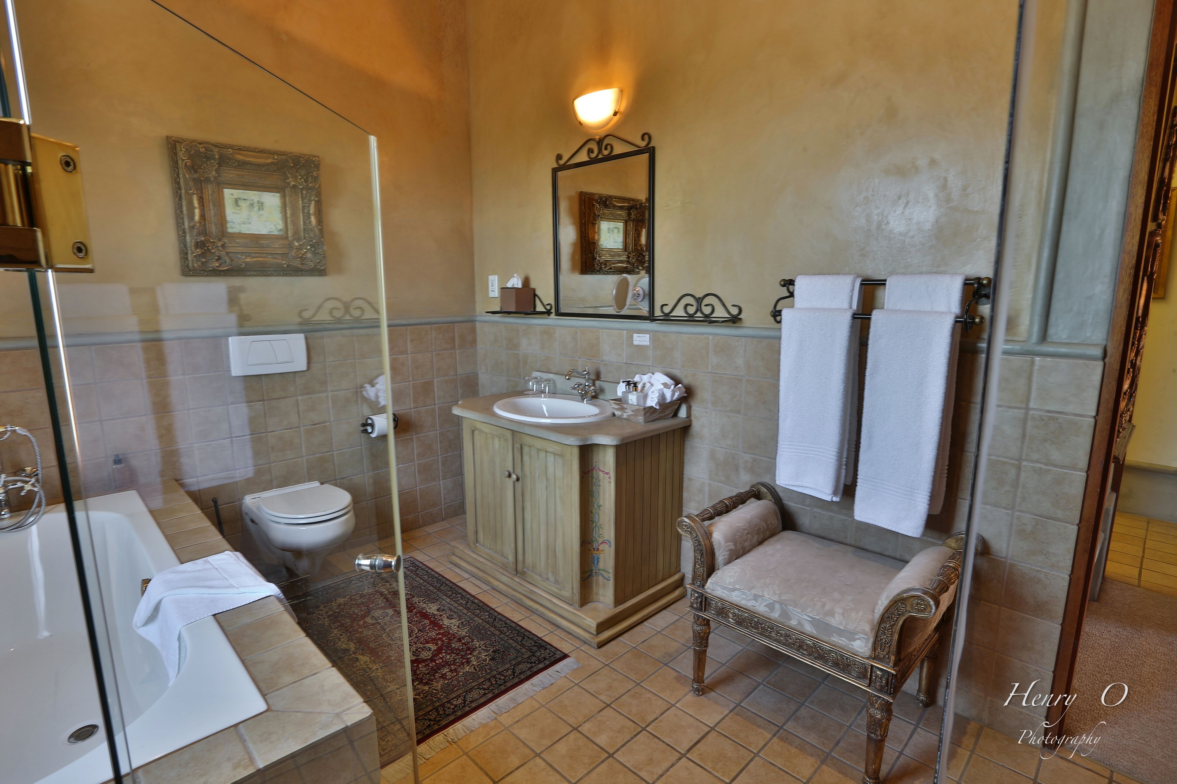 A bathroom with a glass shower enclosure, a sink, a toilet, and a vanity with a chair.