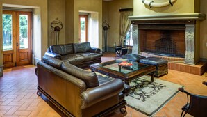A spacious living room with a leather sectional sofa, a glass coffee table, and a fireplace with a decorative cow horn. - Castello di Monte (Pretoria)