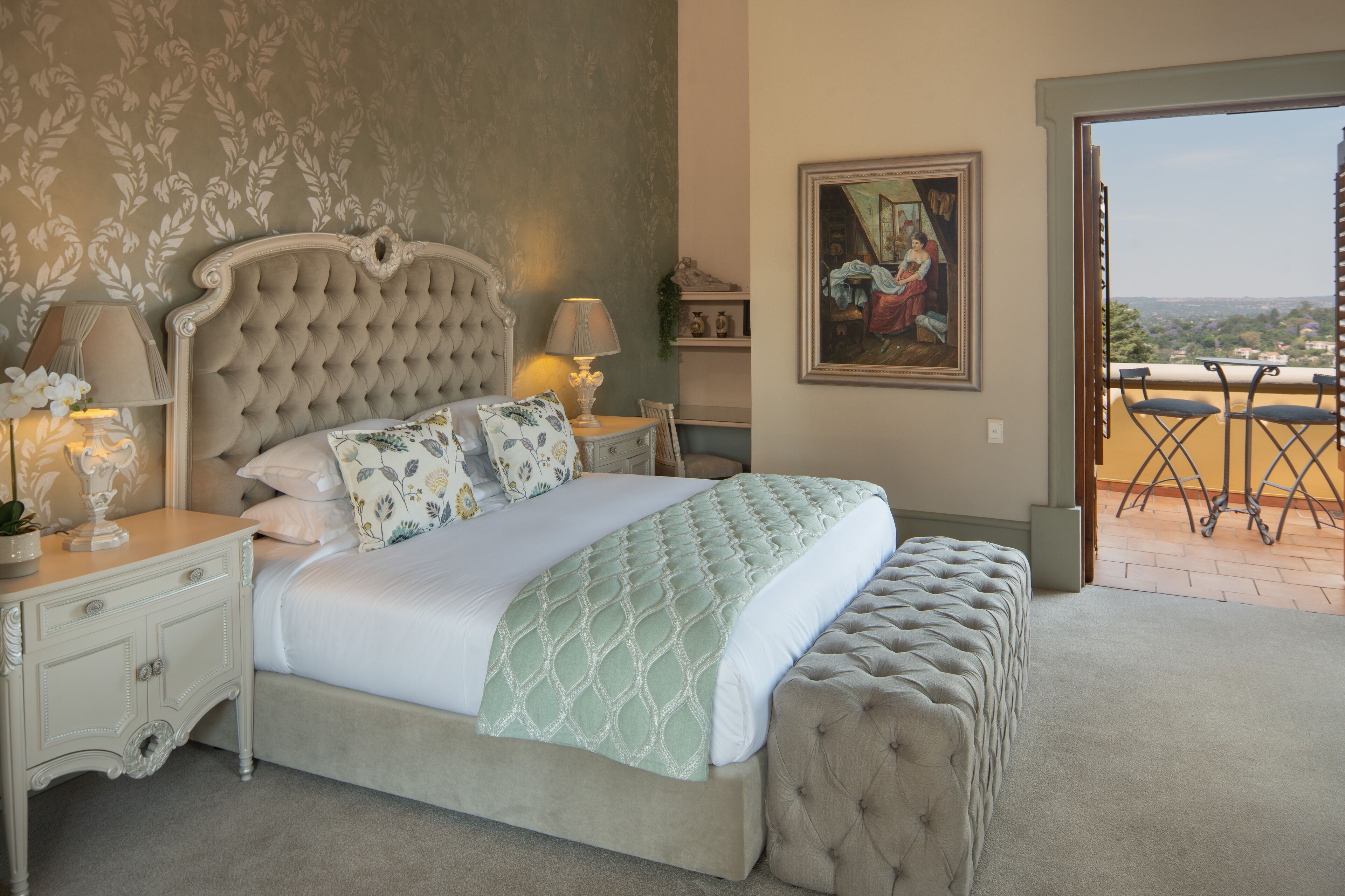 Een slaapkamer met een groot bed, twee nachtkastjes met lampen, een schilderij aan de muur en een balkon met uitzicht.
